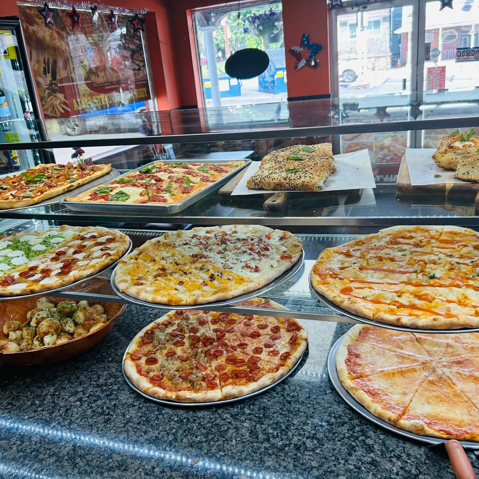 Glass restaurant display case filled with assorted pizzas, stuffed breads, and savory pastries.